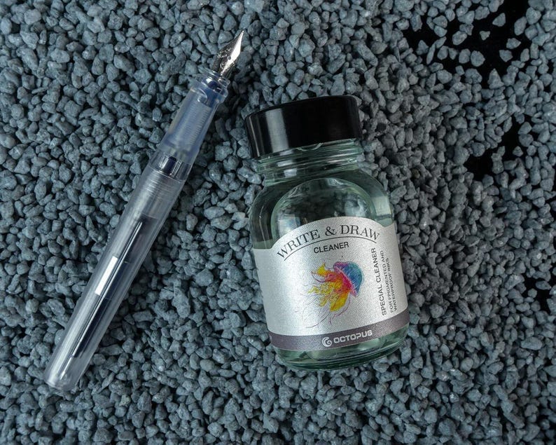 May include: A clear glass bottle with a black cap containing Write & Draw Cleaner, a special cleaner for fountain pens and drawing instruments. The bottle is labeled with a colorful jellyfish illustration and the text "Write & Draw Cleaner" and "Octopus".