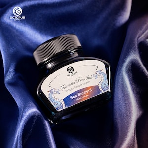 Könnte beinhalten: Eine Glasflasche mit indigo-farbener Füllfederhalter-Tinte mit kupferfarbenem Schimmer. Die Flasche ist mit "Octopus Fluids Fountain Pen Ink Indigo Copper Sheen Sea Serpent 30 ml - 1 fl.oz." beschriftet.