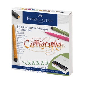 Pu&ograve; includere: Una scatola di 12 Faber-Castell Pitt Artist Pens Calligraphy Studio Box. La scatola &egrave; bianca con un bordo verde e bianco. La scatola contiene un'immagine di una penna e il testo "Calligraphy" in un carattere decorativo. La scatola contiene anche il testo "Creative Studio - Made in Germany".