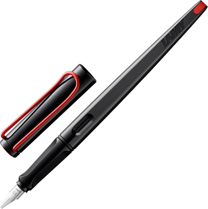 May include: A black fountain pen with a red clip and a black cap. The pen has a silver nib and the word "LAMY" is printed on the cap.