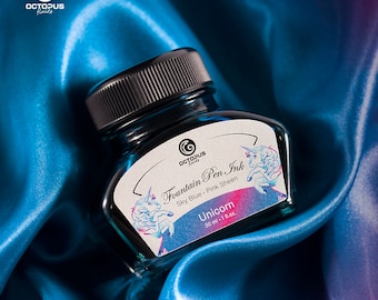 May include: A glass bottle of blue fountain pen ink with a unicorn illustration and the text "Fountain Pen Ink Sky Blue Pink Sheen Unicorn 30 ml - 1 fl.oz."