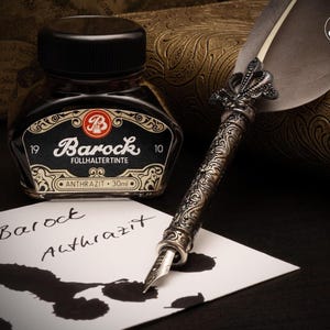 May include: A vintage-style ink bottle and quill pen set. The black ink bottle, labeled "Barock Füllhaltertinte," sits next to a decorative pen with a silver-colored metal handle and a feather. The ink has a volume of 30ml.