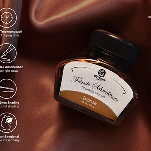 May include: A bottle of bronze fountain pen ink with a black cap. The label reads "Feinste Schreibtinte" and "Bronze". The image also includes text indicating short drying time, quick writing, beautiful shading, and that it is vegan and made in Germany.