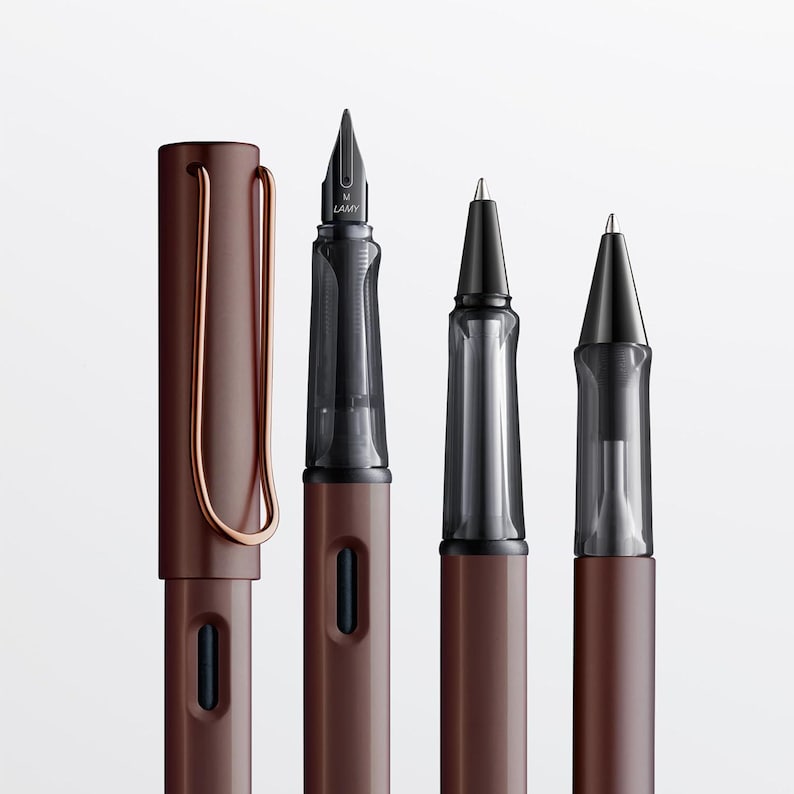 Pode incluir: Quatro canetas na cor marrom com detalhes pretos. As canetas s&atilde;o uma caneta-tinteiro, uma caneta rollerball e duas canetas esferogr&aacute;ficas. A caneta-tinteiro tem um cartucho de tinta transparente e a caneta rollerball tem um corpo transparente. As canetas est&atilde;o todas em fila sobre um fundo branco.