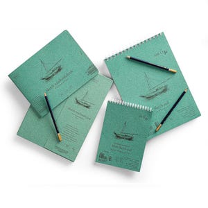 May include: An assortment of green sketchbooks and sketchpads with a sailboat illustration. The sketchbooks are spiral-bound and have the text "Sketch #authenticbook" and "White Sketch pad". Pencils with gold tips are placed on the sketchbooks.