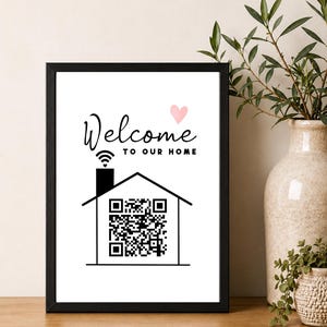 May include: A framed wall sign featuring the text Welcome to our home in black script and block lettering. Below the text is a black line drawing of a house with a chimney emitting a Wi-Fi symbol and a QR code inside the house outline.