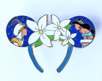 Può includere: Un paio di orecchie da topo blu con un cerchietto bianco. Le orecchie presentano uno sfondo blu con stelle bianche e una scena del film Aladdin. Un orecchio mostra Jasmine e l'altro orecchio mostra Aladdin.