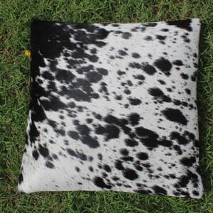 May include: Black and white cowhide pillow with a spotted pattern.