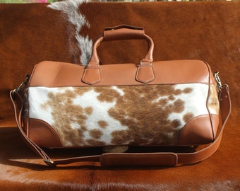 Könnte beinhalten: Eine braune Ledertasche mit Kuhfellmuster. Die Tasche hat einen oberen Griff und einen langen Schultergurt.