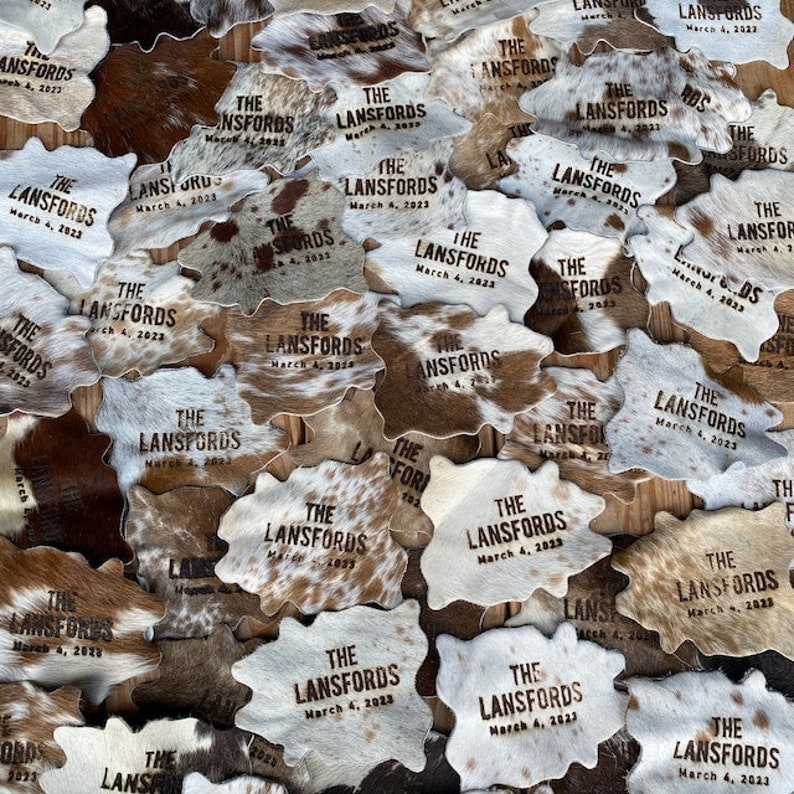 May include: A close-up of a pile of cowhide coasters with the text "The Lansfords" and the date "March 4, 2023" burned into each coaster.