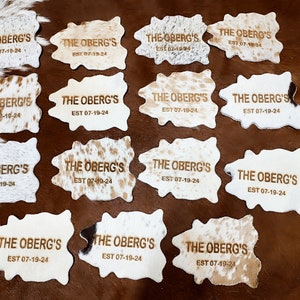 May include: Twelve cowhide rugs with the text "THE OBERG'S EST 07-19-24" embossed in gold lettering.