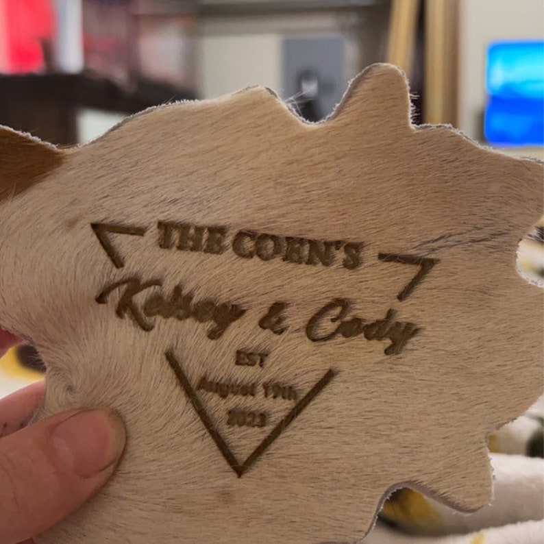 May include: A light brown cowhide coaster with a brown triangle design and the text "The Corn's 7 Kelsey & Cody Est. August 17th 2023"