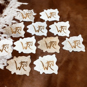 May include: Twelve brown and white cowhide coasters with a gold embossed "WR" logo and a horse head design.