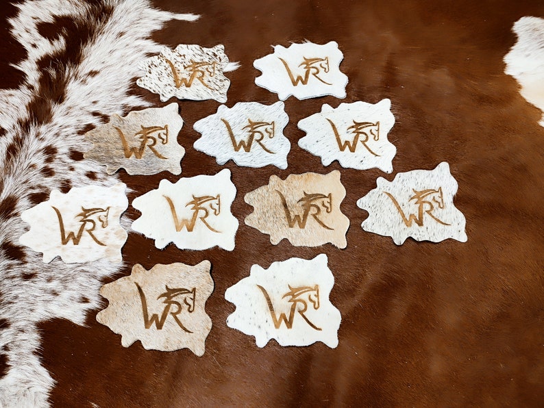 May include: Twelve brown and white cowhide coasters with a gold embossed "WR" logo and a horse head design.