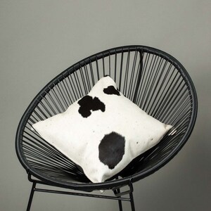 May include: A black and white cowhide pillow on a black wire chair. The pillow has a white background with black spots.
