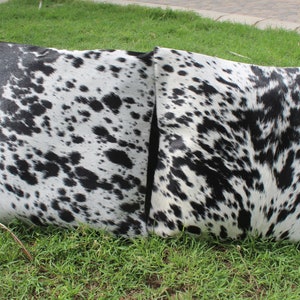 May include: Two black and white cowhide throw pillows with a spotted pattern. The pillows are on a green grassy surface.