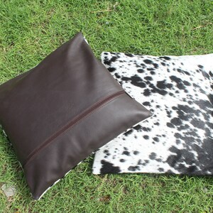 May include: Two decorative throw pillows, one brown leather and one with a black and white cowhide pattern.