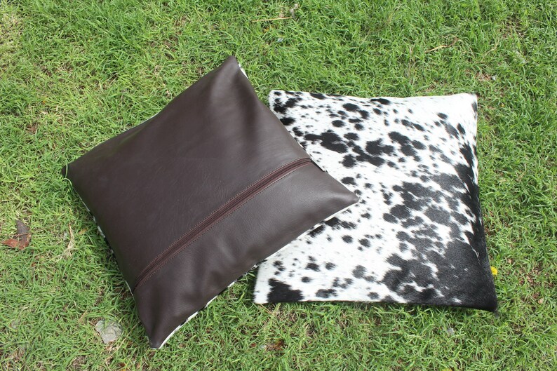 May include: Two decorative throw pillows, one brown leather and one with a black and white cowhide pattern.