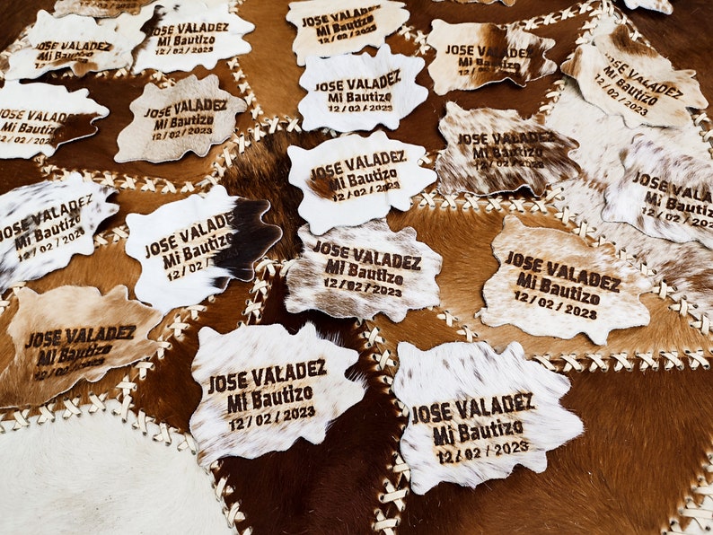 May include: A close-up of several cowhide patches with the text "JOSE VALADEZ Mi Bautizo 12/02/2023" burned into the leather. The patches are arranged in a random pattern and are all the same size.