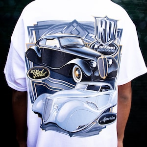 May include: White t-shirt with a graphic print of two vintage cars. The top car is black and says "The Black Pearl" and the bottom car is light blue and says "Aquarius". The graphic also includes the text "RD Customs".