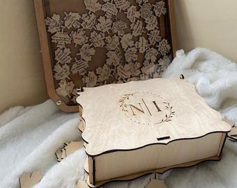 May include: A wooden box with a decorative design and the initials "N I" engraved on the top. The box is open and has a light wood finish. The box is surrounded by small wooden leaves.