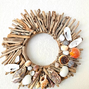 Peut inclure: Une couronne faite de branches de bois flotté avec diverses coquillages attachés. Les coquillages sont dans des tons de blanc, brun, orange et rose.