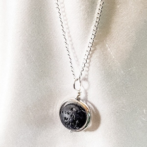 May include: A silver chain necklace with a round pendant featuring a black lava rock.