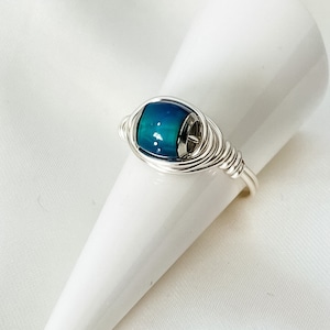 May include: A silver wire wrapped ring featuring a blue and green iridescent glass bead.