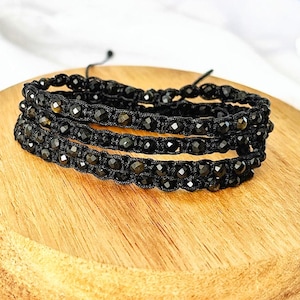 May include: A black beaded bracelet with multiple strands of black beads woven together with black cord.