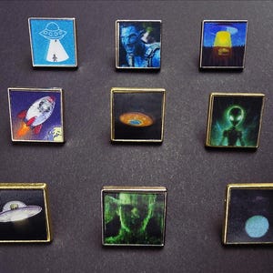 Peut inclure: Une collection de neuf épingles carrées avec des bordures dorées. Chaque épingle présente une image colorée différente liée à l'espace et aux thèmes extraterrestres, notamment des fusées, des ovnis et des figures d'extraterrestres. Les épingles sont disposées sur une surface sombre.