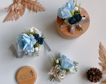 Puede incluir: Tres arreglos florales azules y azul marino de diferentes tamaños. Los arreglos están en cajas de madera y un pequeño círculo de madera con el texto "A Blossoming Life, FYNW Flower Studio UK".