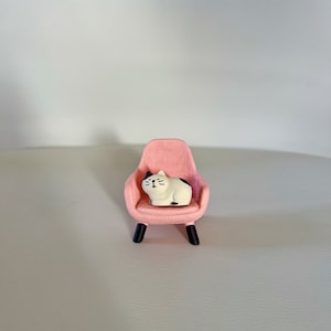 Op de afbeelding: Een roze fauteuil met een wit en zwart kattenbeeldje dat op de zitting zit.