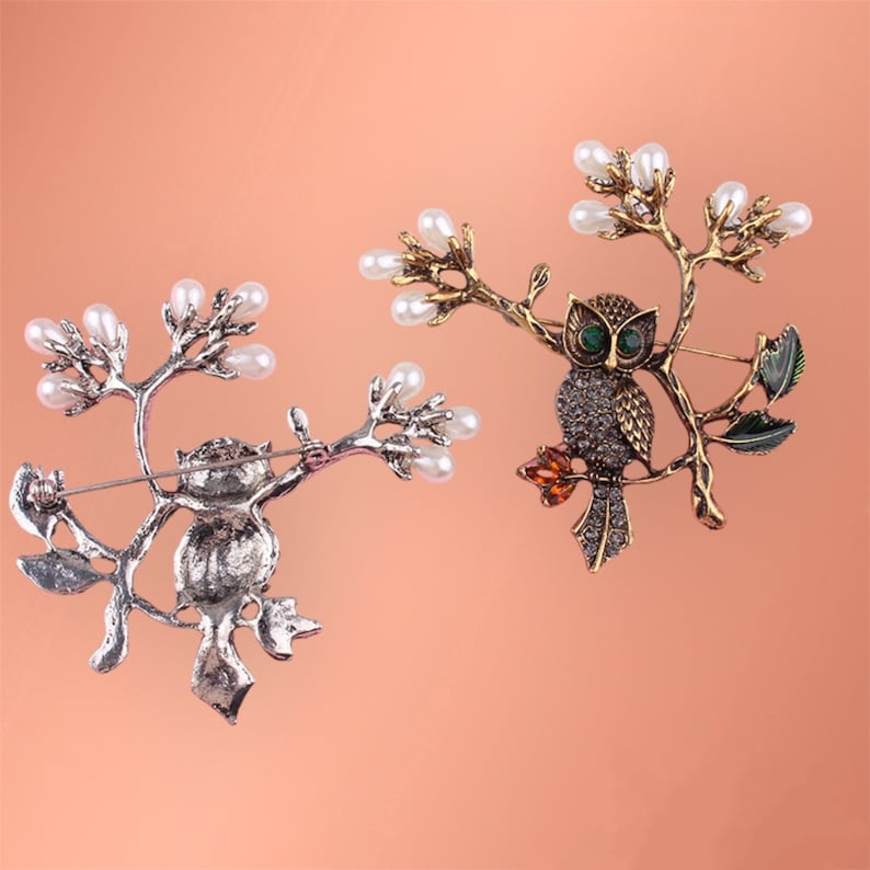 May include: Two owl brooches with pearl accents. One owl is silver with a brown owl, the other is gold with a green-eyed owl.