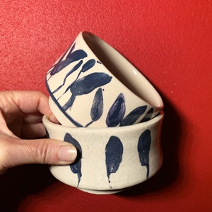 Peut inclure: Deux bols en céramique blanche avec des motifs de feuilles bleues. Les bols sont empilés l'un sur l'autre.