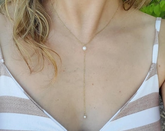 May include: A delicate gold-tone necklace with a Y-shaped design. The necklace features a small, round, white pearl at the top and a dangling pearl at the end of the chain. The necklace is worn against a striped top.