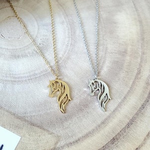 May include: Two horse head necklaces, one gold and one silver, on a wooden surface.