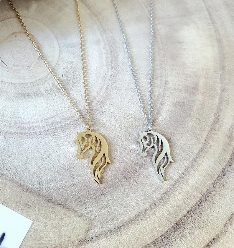 May include: Two horse head necklaces, one gold and one silver, on a wooden surface.