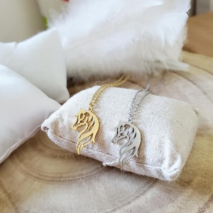May include: Two horse head necklaces, one gold and one silver, on a beige fabric surface.