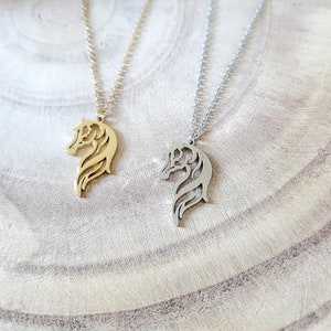May include: Two horse head necklaces, one gold and one silver, on a wooden surface.