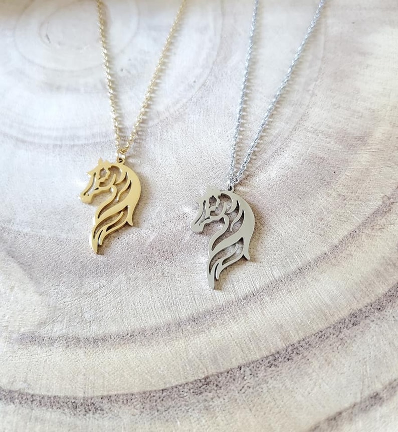 May include: Two horse head necklaces, one gold and one silver, on a wooden surface.