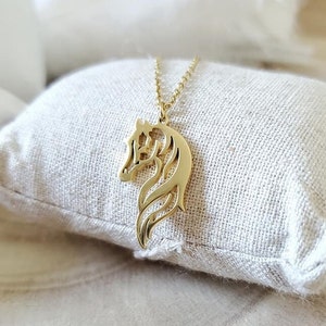 May include: A gold-toned necklace featuring a horse head pendant. The pendant is a cut-out design, with the horse's mane and tail flowing behind it.