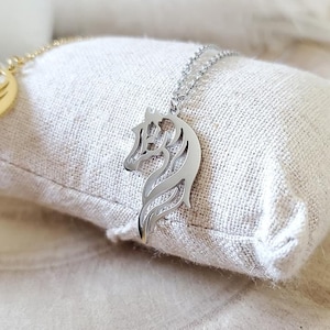 May include: A silver horse head pendant necklace on a white fabric background.
