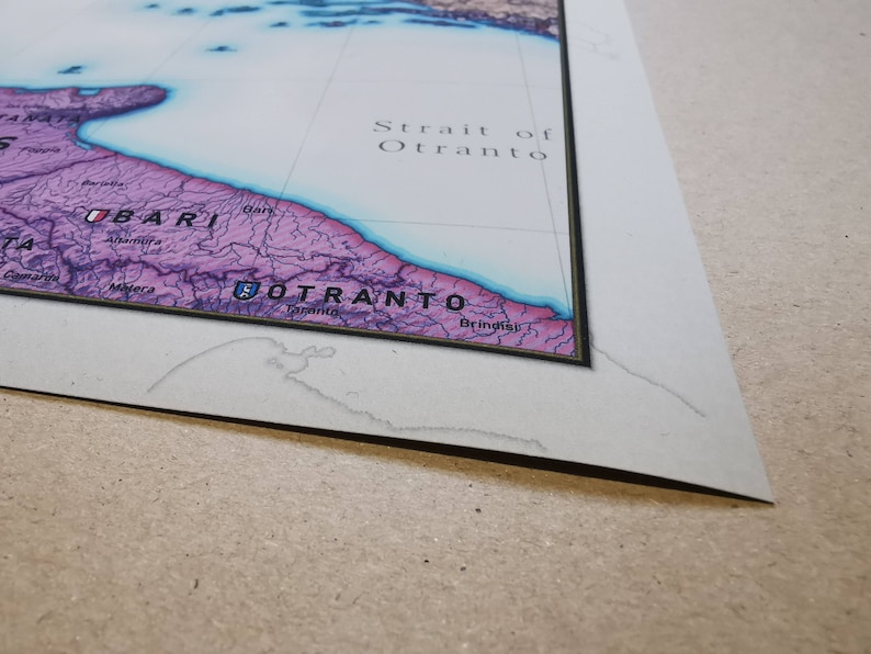 May include: A close-up of a map showing the Strait of Otranto, a body of water separating Italy and Albania. The map is printed on paper and framed with a black border.