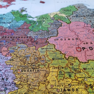 May include: A vintage map of Europe with detailed borders and city names. The map is printed on paper and has a worn, aged look. The map is in shades of brown, green, pink, and blue.