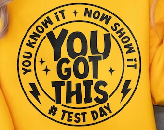 Puede incluir: Una sudadera amarilla brillante con un diseño circular negro que dice "YOU KNOW IT + NOW SHOW IT, YOU GOT THIS, # TEST DAY". La sudadera es de manga larga y tiene cuello redondo.