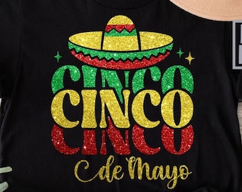 Puede incluir: Camiseta negra con un diseño brillante dorado, verde y rojo que dice "Cinco Cinco Cinco de Mayo" con un sombrero encima.