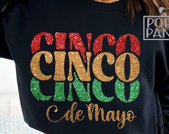 Może przedstawiać: Czarna bluza z błyszczącym złotym, czerwonym i zielonym wzorem z napisem "Cinco de Mayo".