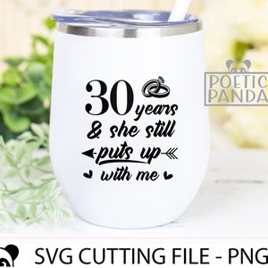 May include: White stainless steel tumbler with a black design that says "30 years & she still puts up with me" with two rings and an arrow. The tumbler is sitting on a green leafy surface.