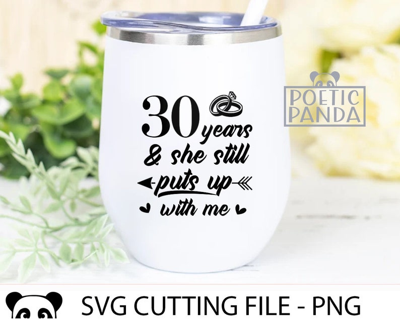 May include: White stainless steel tumbler with a black design that says "30 years & she still puts up with me" with two rings and an arrow. The tumbler is sitting on a green leafy surface.