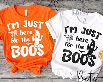 May include: Two t-shirts, one orange and one white, with the phrase "I'M JUST here for the BOOS" printed in black. The design includes a ghost, spiderweb, and bat, perfect for Halloween.